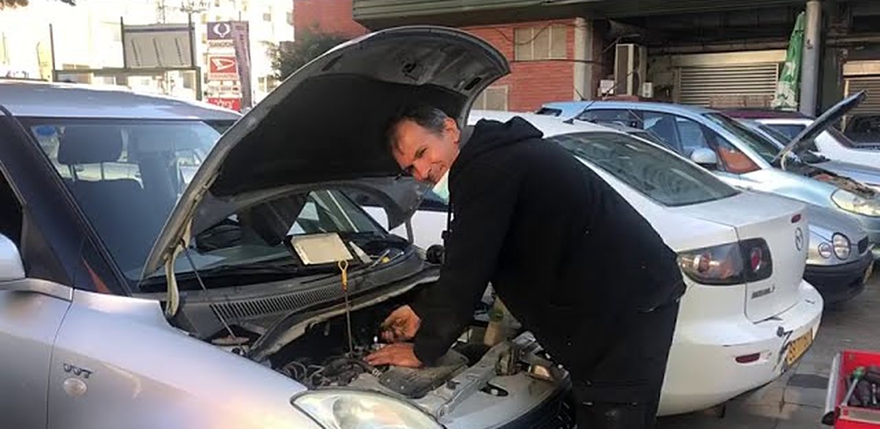 מכונאי עובד בתוך תא המנוע של רכב, בחצר המוסך
